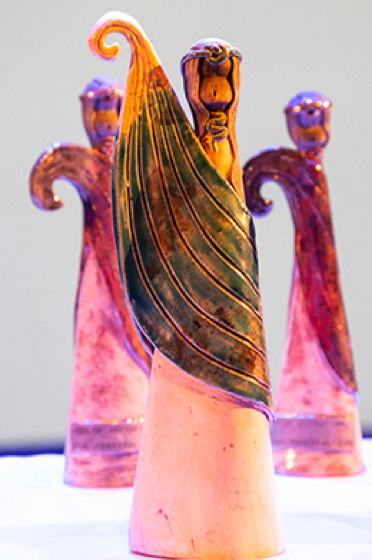 Photo of one of a group of our trophies commissioned from Rachel Quinn. There are three separate figures in this photo, showing female celtic figures with a shawl which seems to blow and curl in the wind like a sea wave. The lighting shows up lovely red/pink hues on the pieces.
